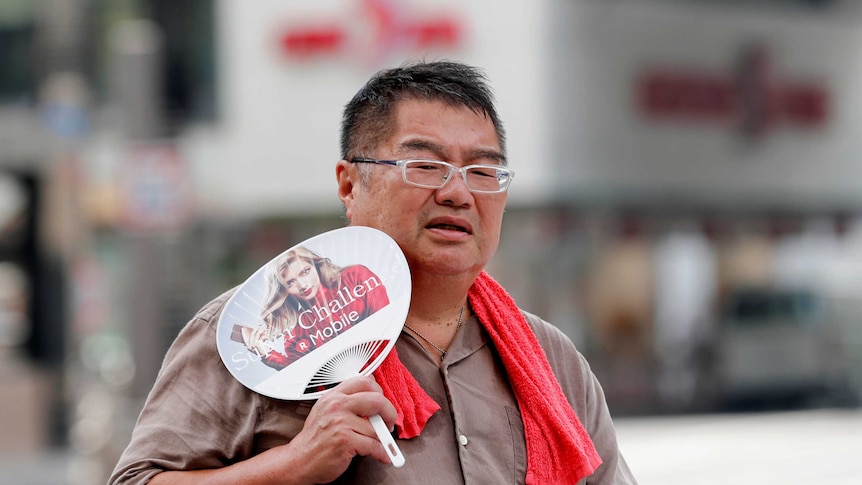 A man uses a fan as he walks on a street in Tokyo.