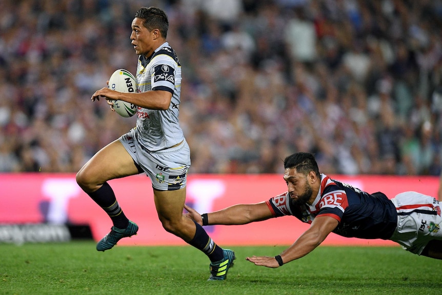Te Maire Martin, in North Queensland Cowboys kit, runs towards the tryline while a Roosters player dives towards him