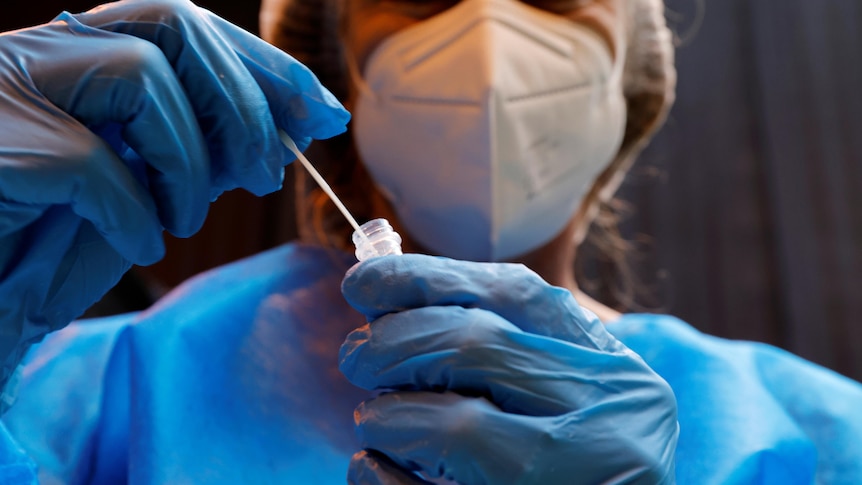 A woman in full PPE puts a swab in a sample tube.