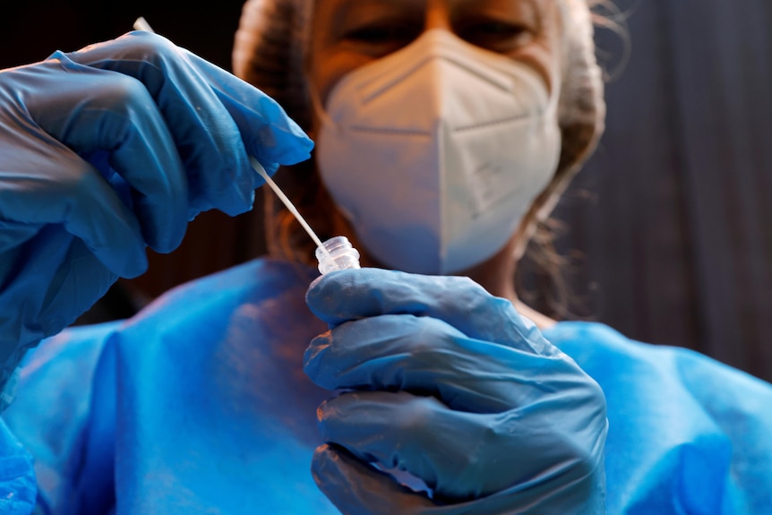 A woman in full PPE puts a swab in a sample tube.