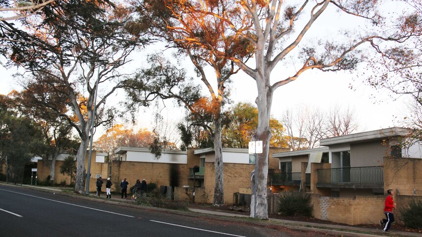People stand outside Jerilderie Court unit complex, among the trees.