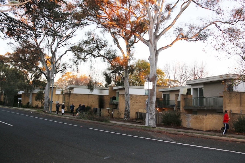 People stand outside Jerilderie Court unit complex, among the trees.