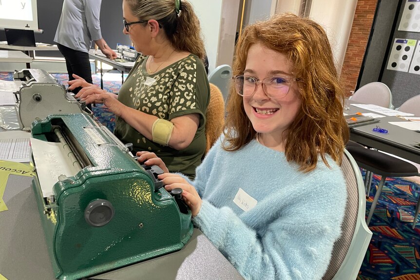 A girl with red hair smiles as she uses a Brailler
