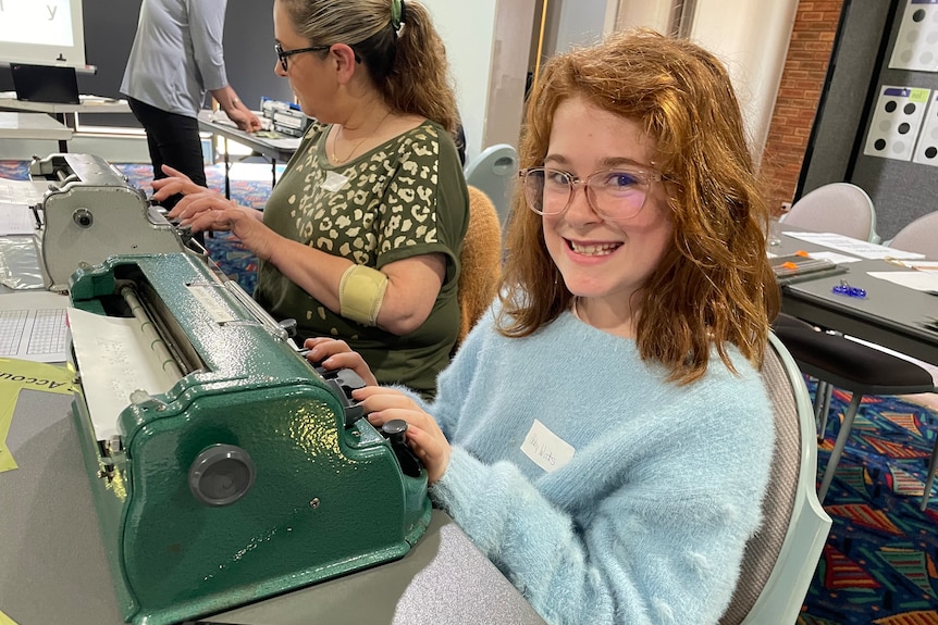 A girl with red hair smiles as she uses a Brailler