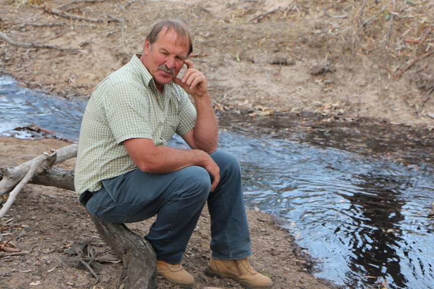 A farmer sitting beside a dry creek as it fills with water