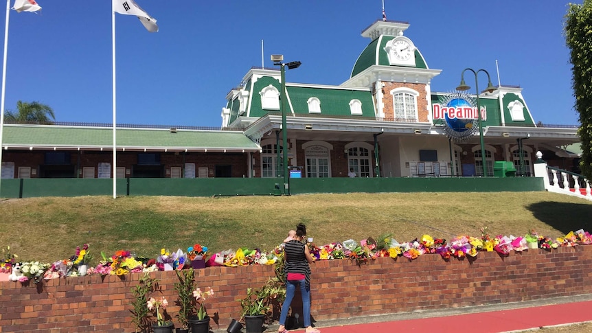 A woman holding a baby looking at floral tributes outside Dreamworld