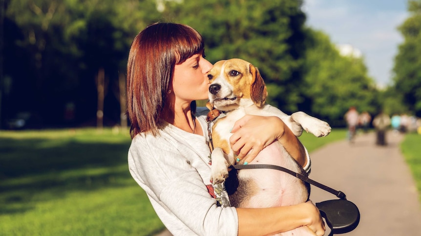 Woman hugging and kissing her dog in the park for a story about choosing not to have children.