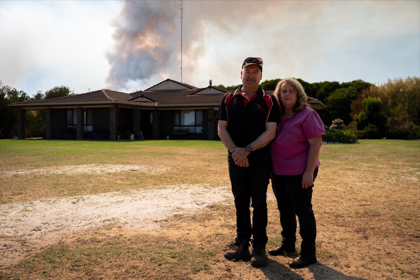 Debbie Woodley and Nigel Johns standing out the front of their house, smoke can be seen in the background.