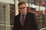 A man wearing a suit and sunglasses walks out of a court