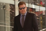 A man wearing a suit and sunglasses walks out of a court