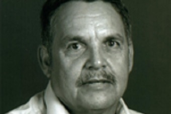 Headshot of a man wearing a white shirt against a black background.