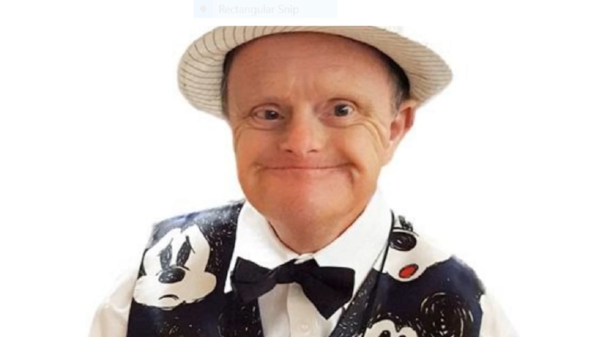 A man of small stature wearing a novelty waistcoat and a hat, smiling broadly.