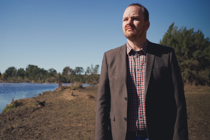 A mayor stands beside a flood-damaged river