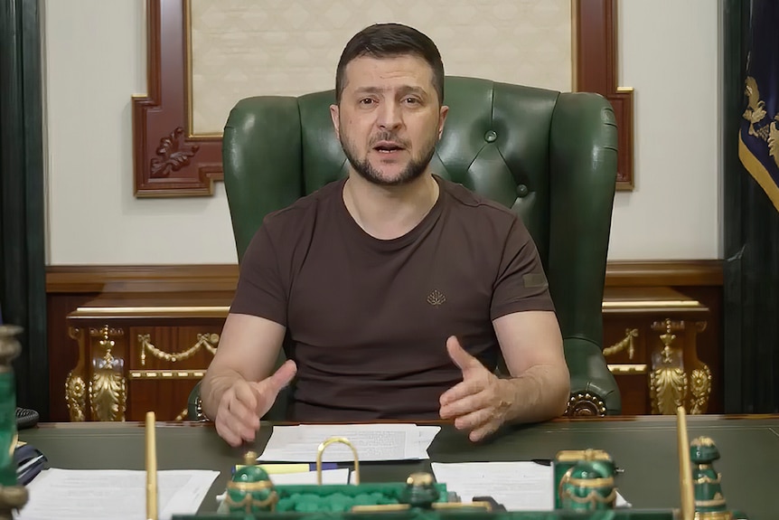 Volodymyr Zelenskyy addresses the camera, sitting at a desk in a chair.