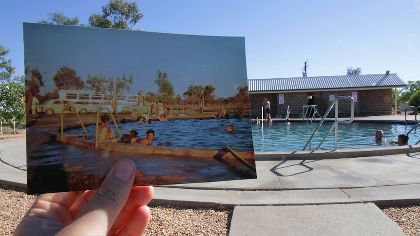 An old photo of the Bore Baths is held up in front of the bore baths as they appear today.