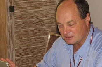 David Archibald sits at a desk in a blue shirt with a computer