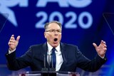 A photo of NRA CEO Wayne LaPierre speaking at a conference with a blue backdrop.