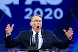 A photo of NRA CEO Wayne LaPierre speaking at a conference with a blue backdrop.