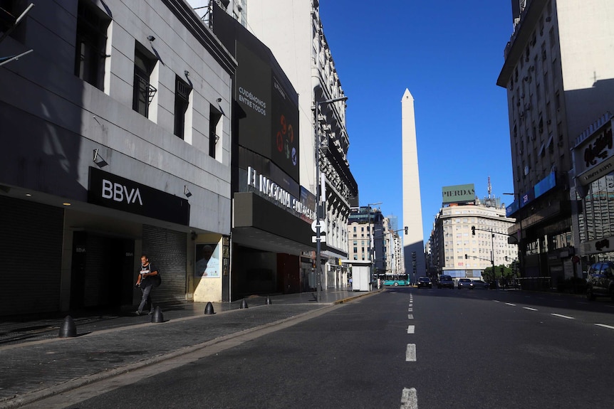One man walks down an empty city street in Buenos Aires Argentina, with an obelisk in the background.