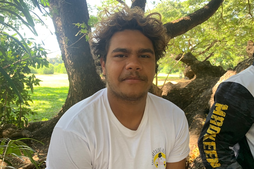 A man wearing a white tshirt looks directly into the camera.