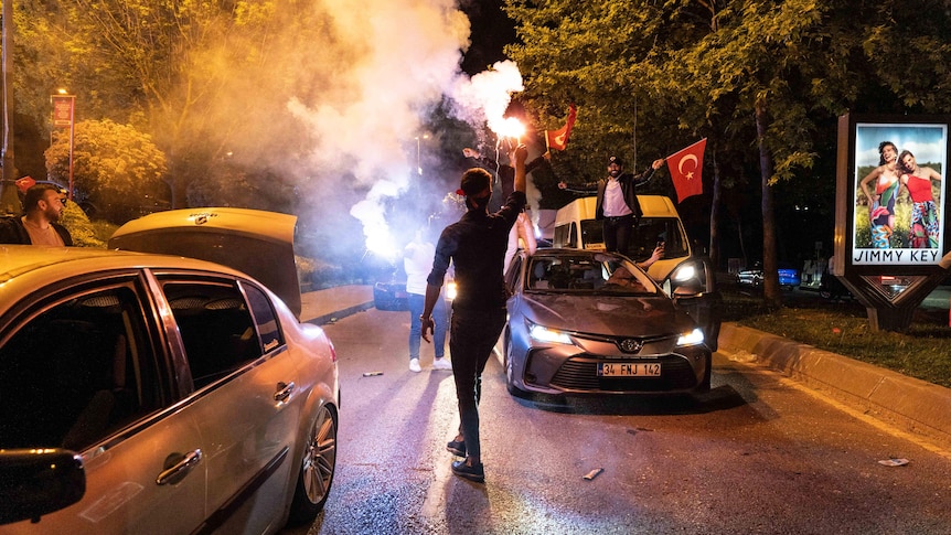 A man with a smoking flare walks down a crowded street at night