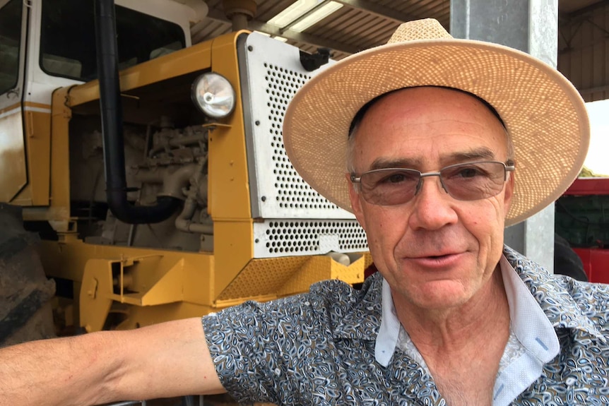 Man in straw hat stands in front of old yellow and white tractor