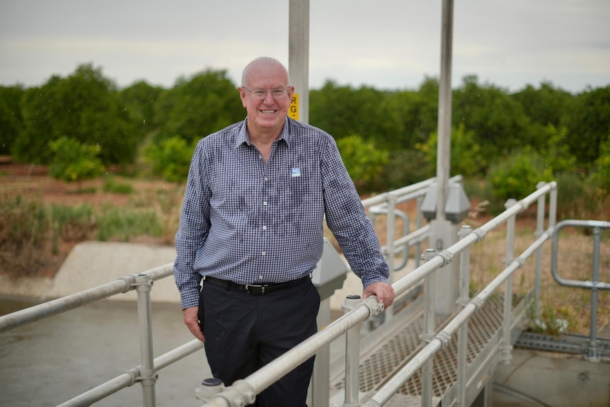 Man wearing a checked blue shirt and glasses standing on a metal bridge.