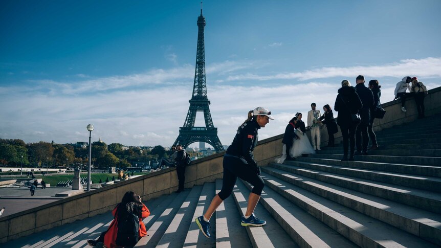 Mina Guli walking up outdoor, concrete steps with the Eiffel Tower in the distance