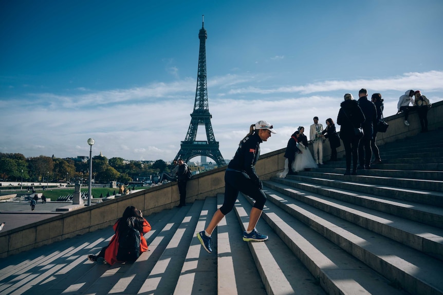 Mina Guli walking up outdoor, concrete steps with the Eiffel Tower in the distance