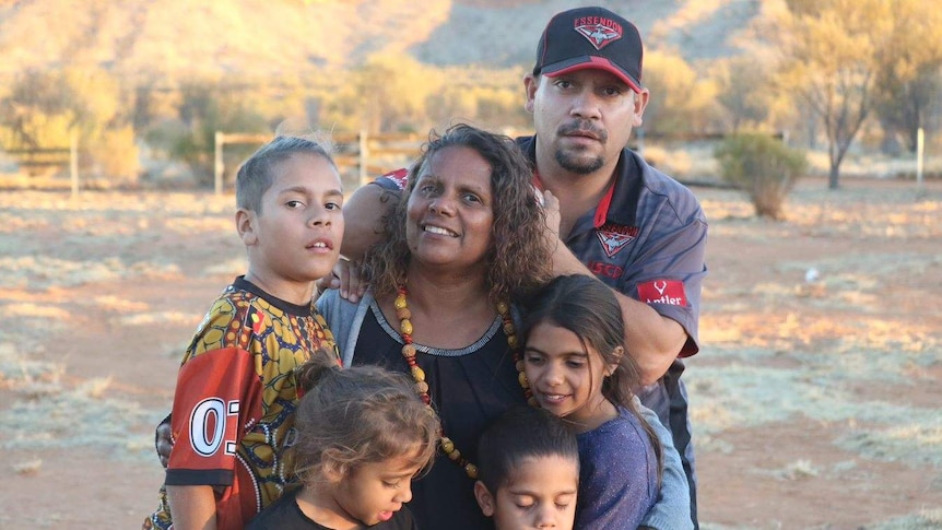 Indigenous family pose for family portrait in outback setting.