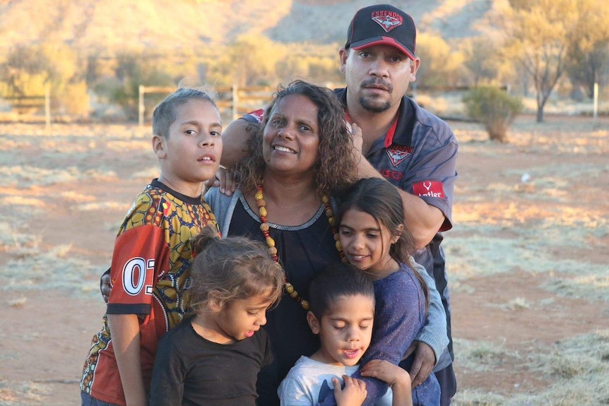 Indigenous family pose for family portrait in outback setting.