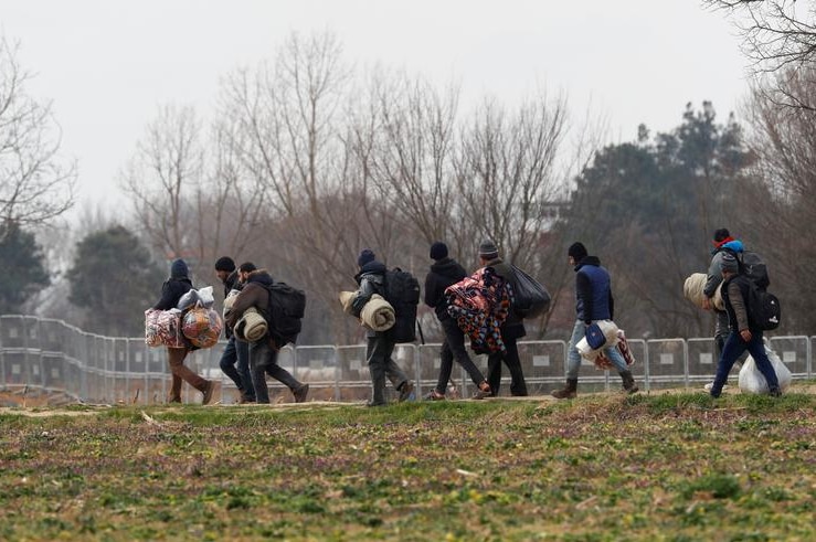 Migrants carrying their belongings walking through a field.