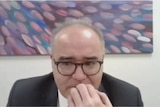 A man in a suit and spectacles biting his nails
