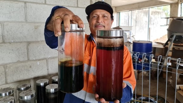 A man in a high vis shirt is holding two canisters of liquid