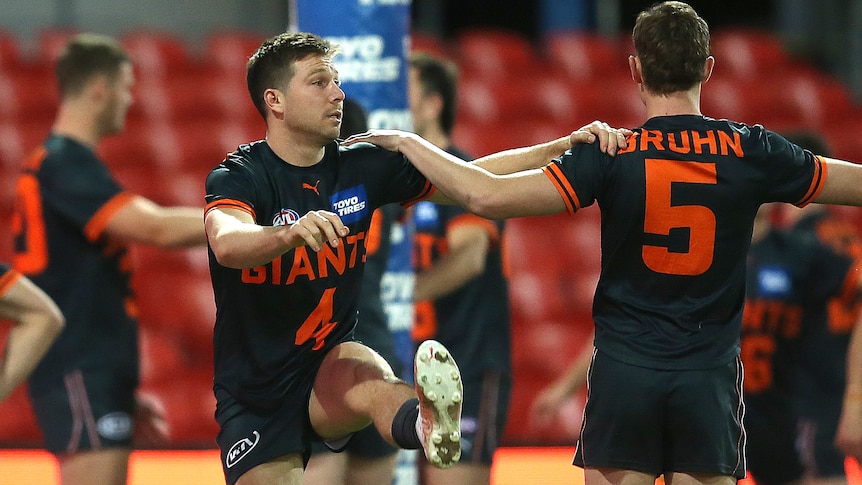GWS' Toby Greene holds onto his teammate's shoulder as he stretches his leg with a high kick. 