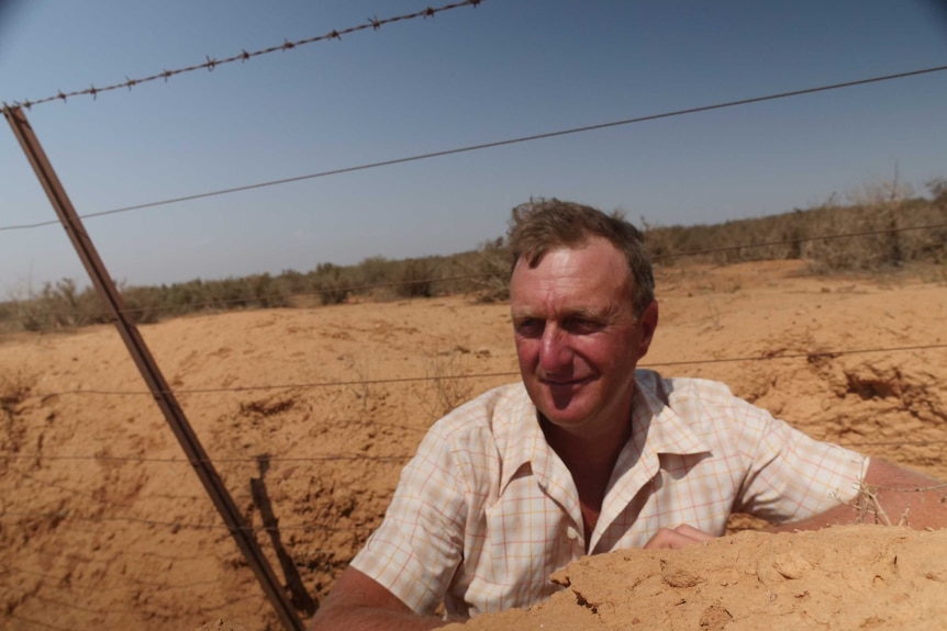 A farmer stands in a wombat hole so deep almost his entire body is hidden.