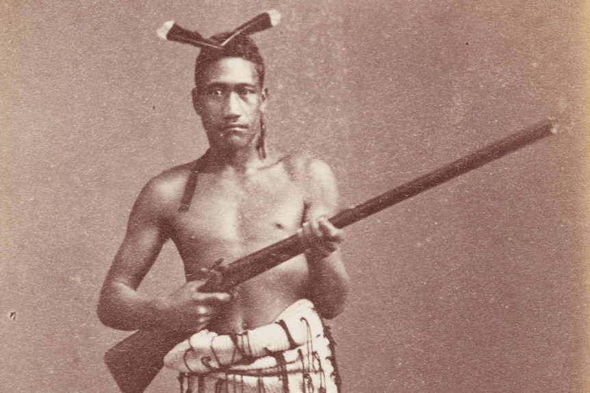 Old photograph of a Maori man in traditional dress holding a musket 