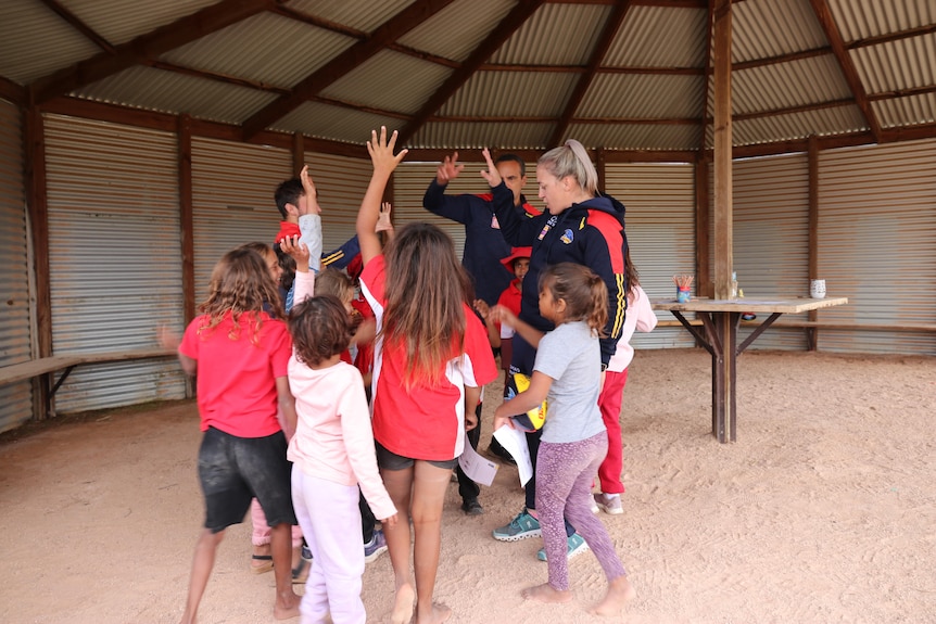 A huddle of laughing students and Crows staff gather with their hands in the air.