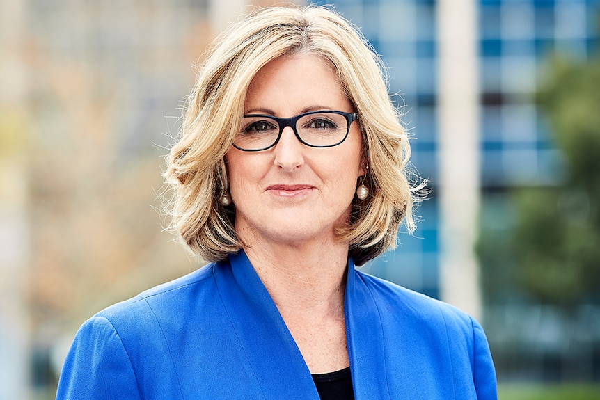 A woman with short blonde hair wearing glasses and a blue jacket