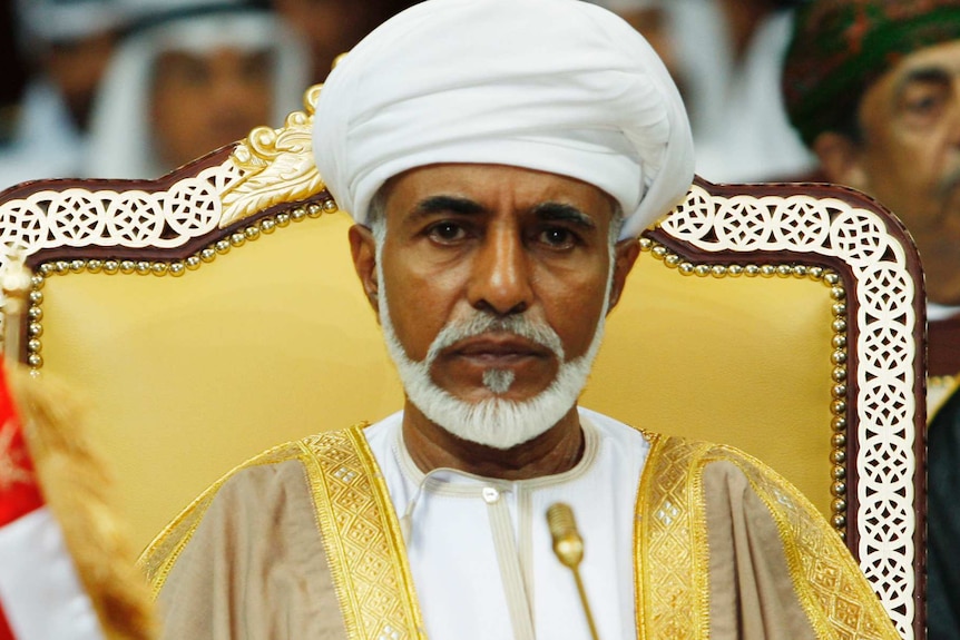 Sultan Qaboos bin Said sits on a yellow-backed chair wearing a white turban and a gold-trimmed tunic.