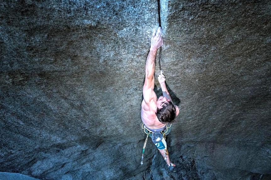 A photo looking down on a  rock climber clinging to a rock crevice.