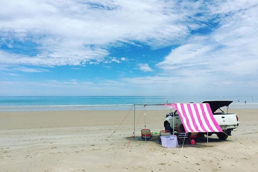 A car and canvas canopy on a wide sandy beach.