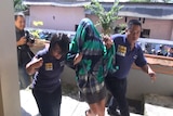 Australian woman Sara Connor wears a sarong over her head as she is escorted to a Bali hospital.