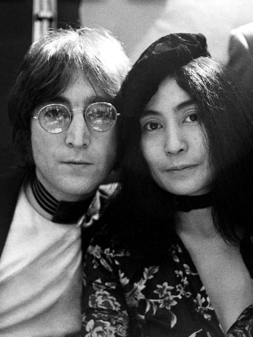 A black and white photo from the 70s of John Lennon, a man with long hair and glasses & Yoko Ono, a Japanese woman in a beret 