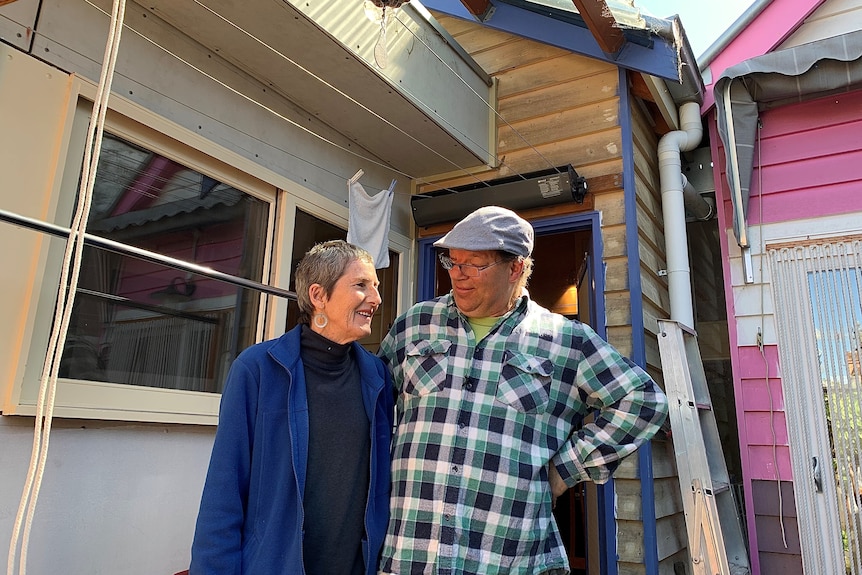 Rowan White and Sue Nash stand in front of their home, looking at each other.