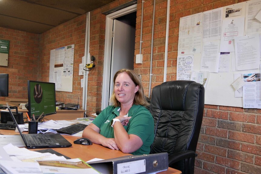 A woman in a green shirt sits at a desk in an office.