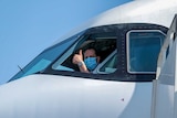 A pilot in a face mask giving the thumbs up out the window of the plane