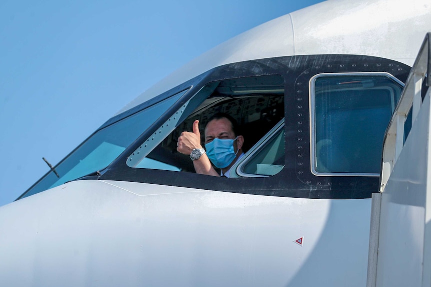 A pilot in a face mask giving the thumbs up out the window of the plane