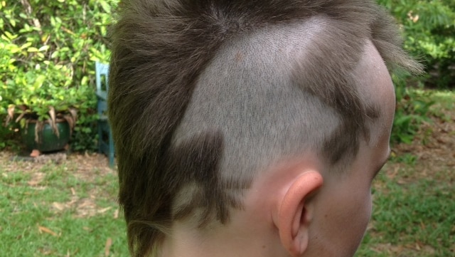 A young boy with a lizard shaped design shaved into his short head of hair.