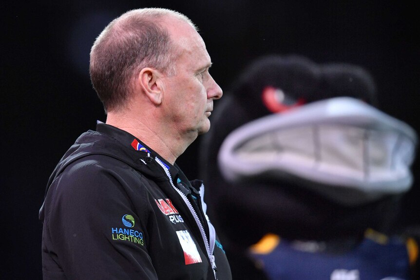 Ken Hinkley looks off in the distance with a giant crow mascot in the background